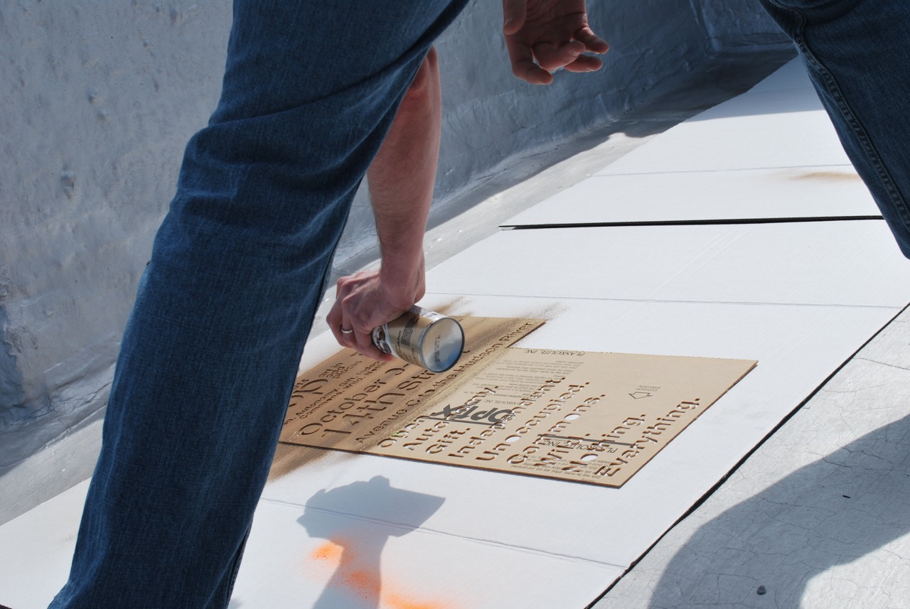 Spray painting a sign for AIOP:Free on a rooftop