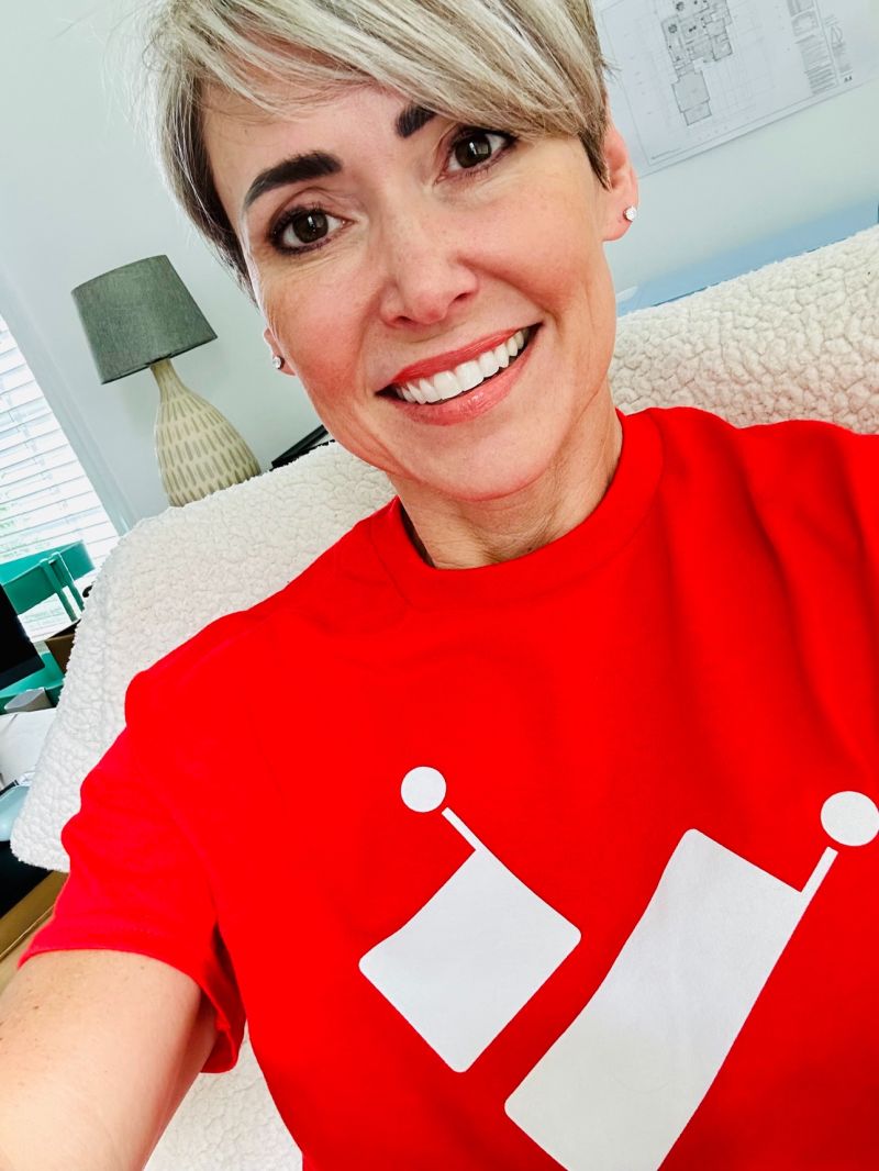 Robin Pugh, CEO of Intelligence for Good wearing a bright red Intelligence for Good T-shirt showing the logo of a heart with dots on each corner. 